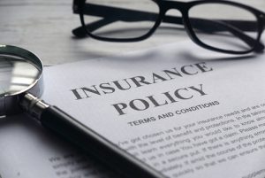 insurance policy laying on desk with a pair of glasses and a magnifying glass laying next to it cybersecurity insurance