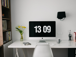 white desk and chair with a computer screen on desk reflecting time of 13 09