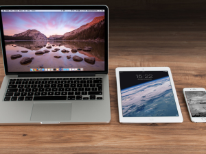 laptop, tablet and phone laying on wooden desk