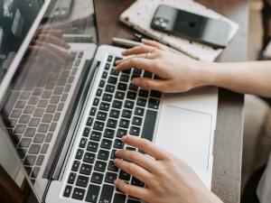 Laptop keyboard with a female typing on it with a apple iphone laying next to keyboard