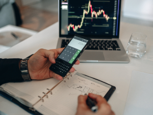 Business laptop on desk with man holding a cellphone with one hand entering info into a notebook CD Technology